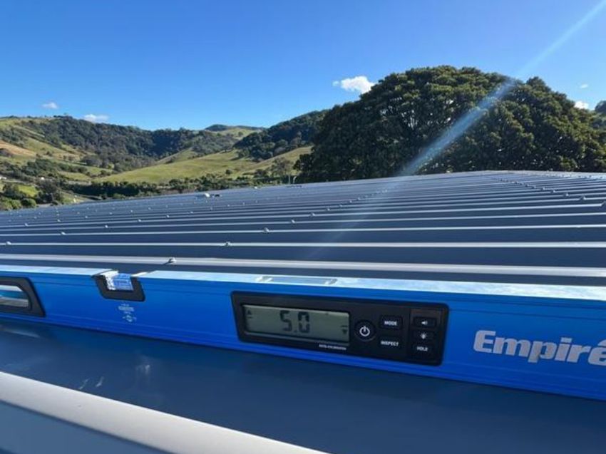 Digital level resting on steel roof sheeting, with green hills behind