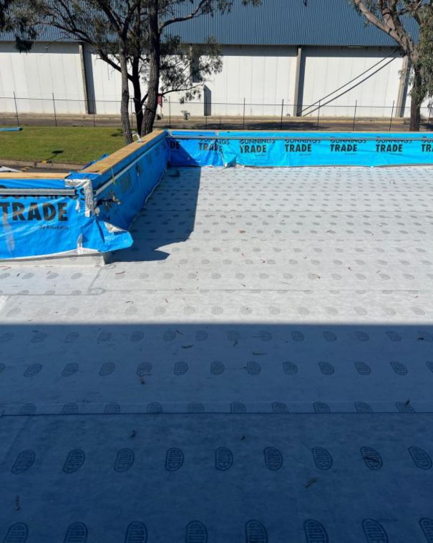 Balcony covered in new grey sheet membrane, with building and trees behind