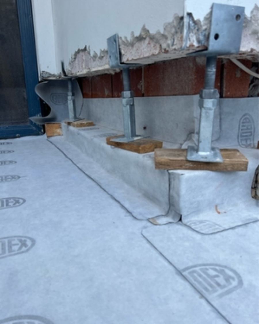 Wall propped on steel acrow props with brick courses removed and membrane flashing installed at the base