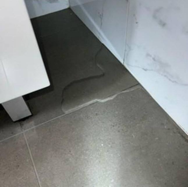 Water spreading across bathroom floor tiles near the door