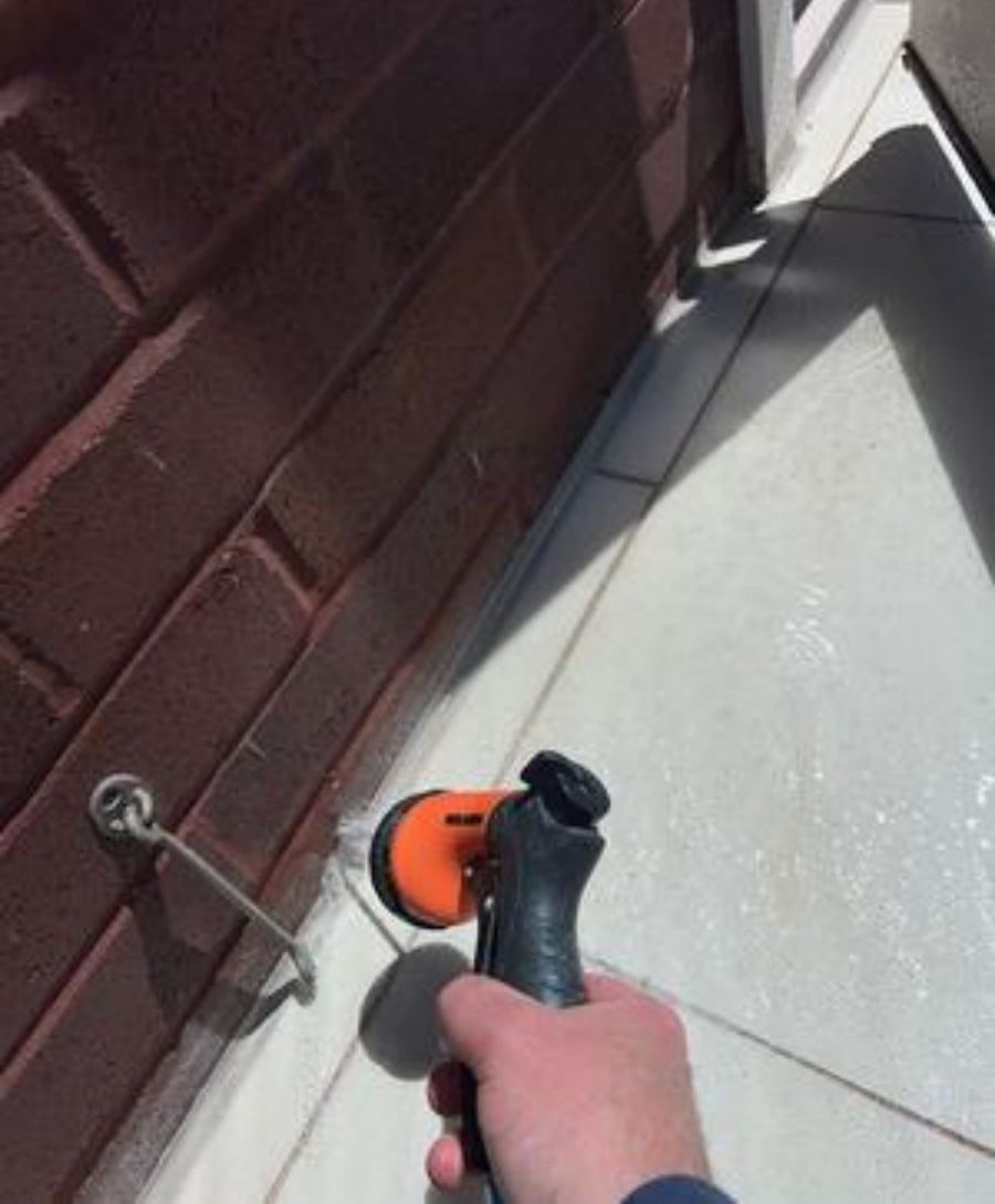 Garden hose spraying water at a missing mortar joint at the base of a brick wall