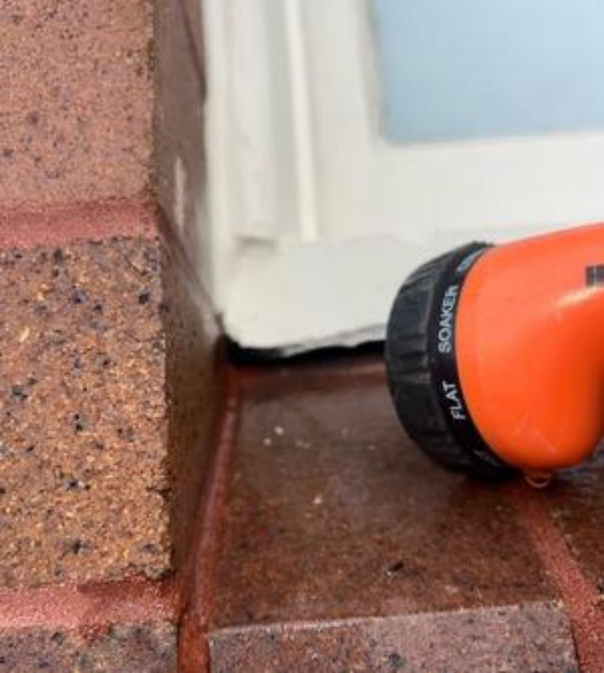 Hose nozzle directing water into the gap under a window sill